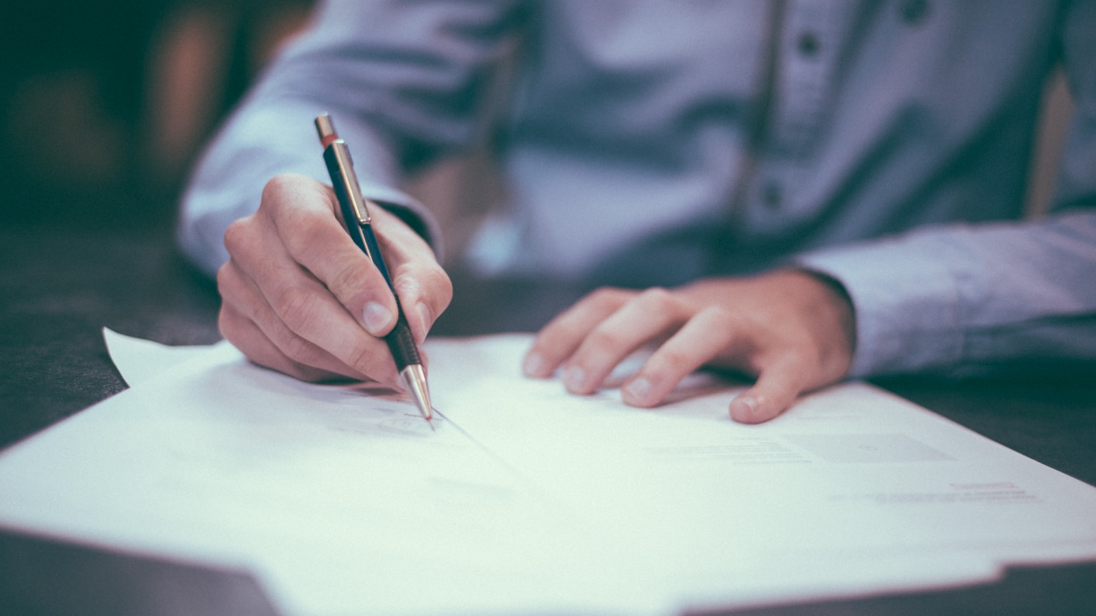 A person sitting at a wooden desk with papers and a calculator under soft light