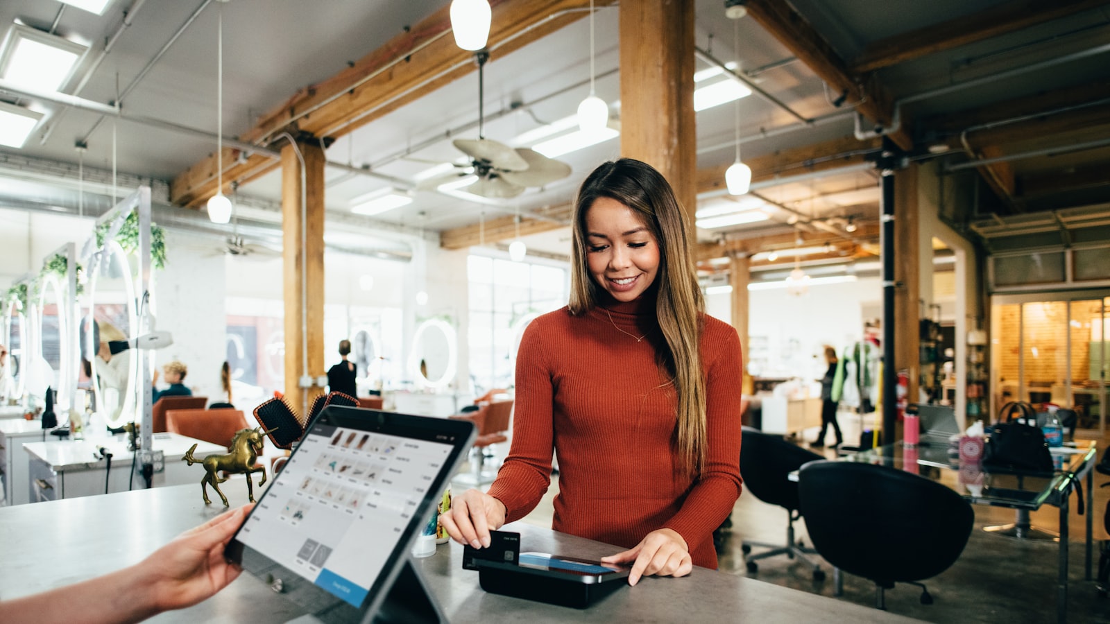 A person working at a laptop on a wooden desk beside a notebook and coffee