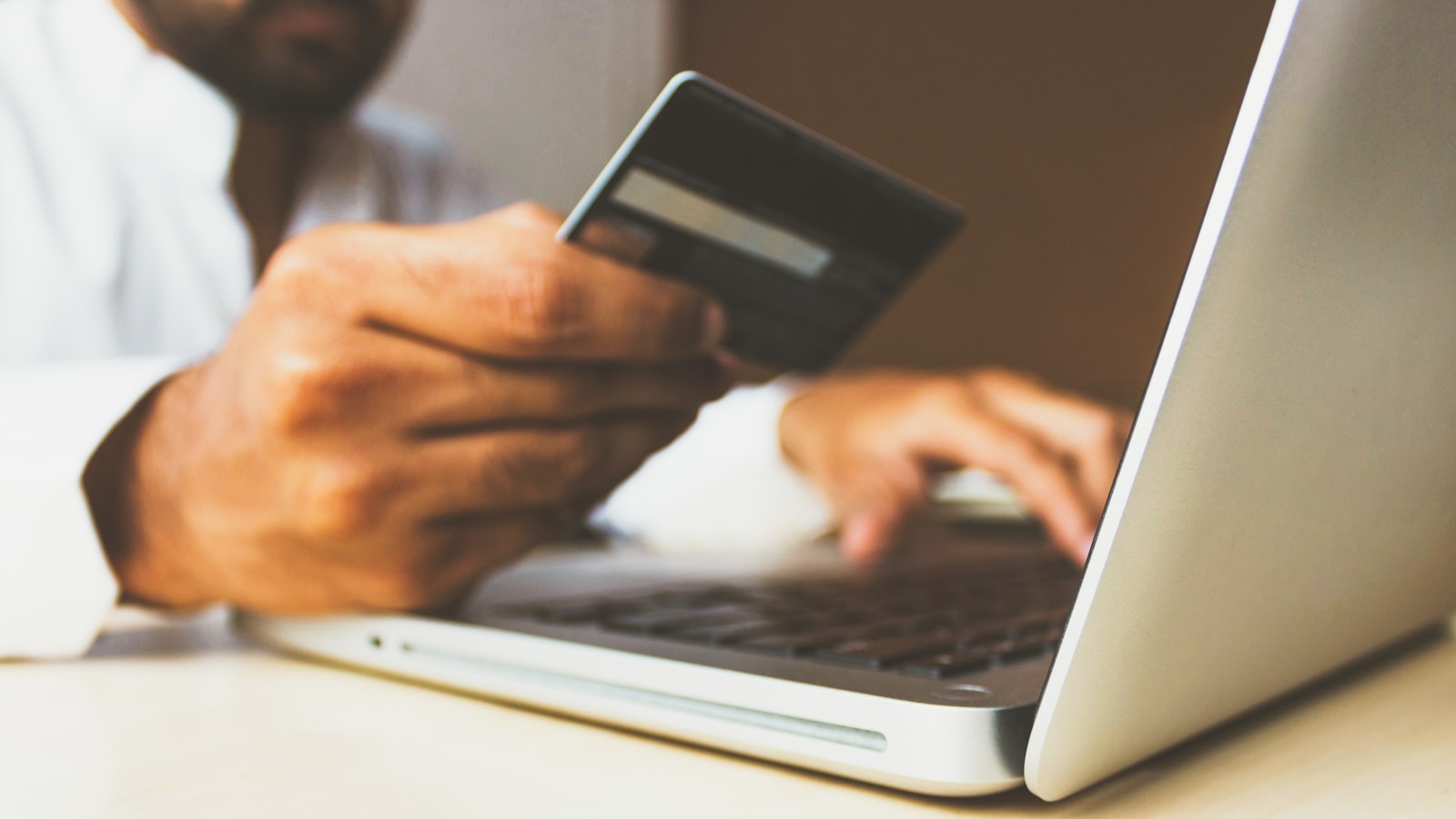A person holding a bank card while looking at a laptop screen at a kitchen table