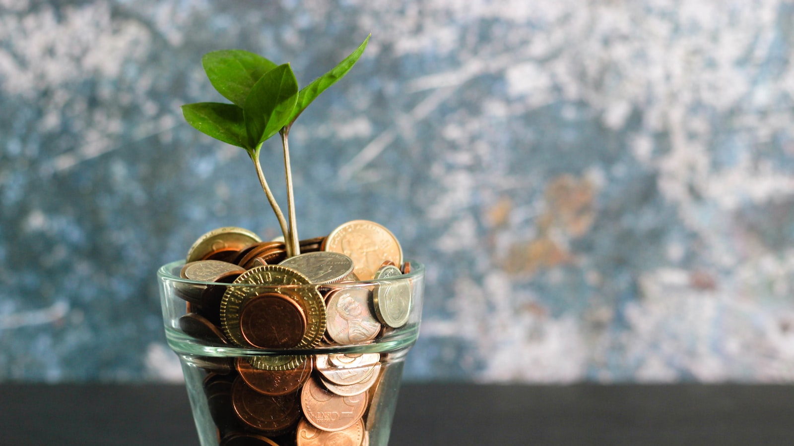 A jar of coins beside a notebook and pen on a wooden desk