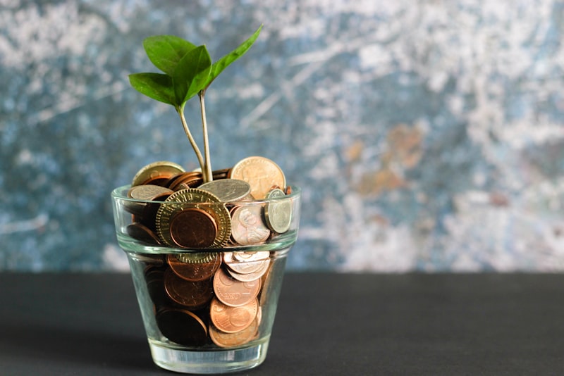 A jar of coins beside a notebook and pen on a wooden desk